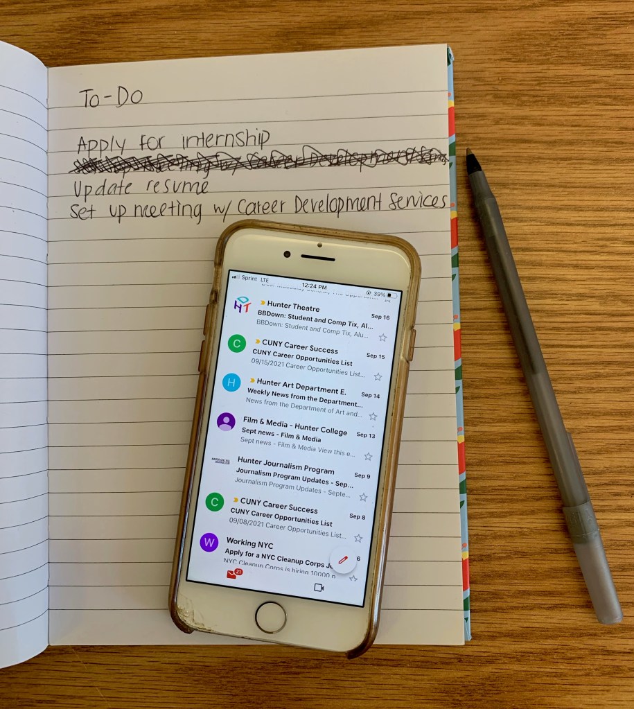 A to-do list in notebook says apply for internship, update resume, set up meeting w/ career development services. Phone on notebook shows Gmail app opened with newsletters from Hunter Theatre, CUNY Career Services, Hunter Art Department, Hunter Film & Media, Hunter Journalism and Working NYC.